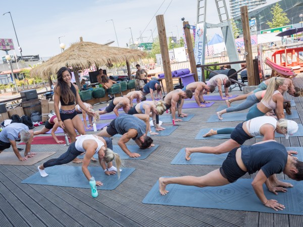 Group of people practicing yoga outdoors on wooden deck.
