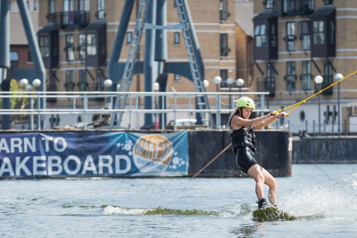 Person wakeboarding near docks with 'Learn to Wakeboard' banner.