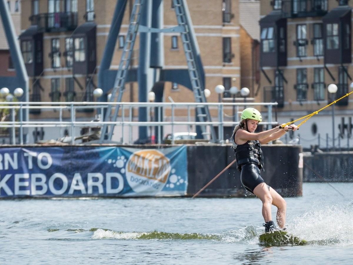 Person wakeboarding near docks with 'Learn to Wakeboard' banner.