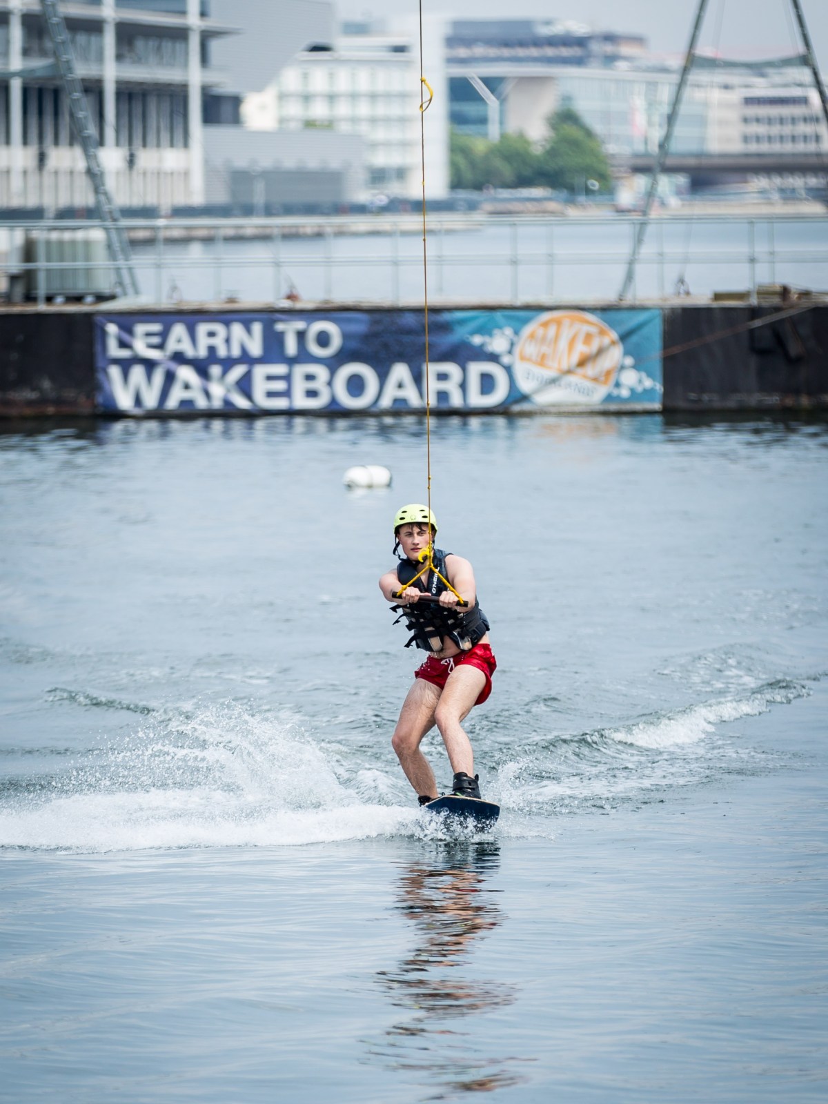 Person wakeboarding on a waterway wearing a helmet and vest.
