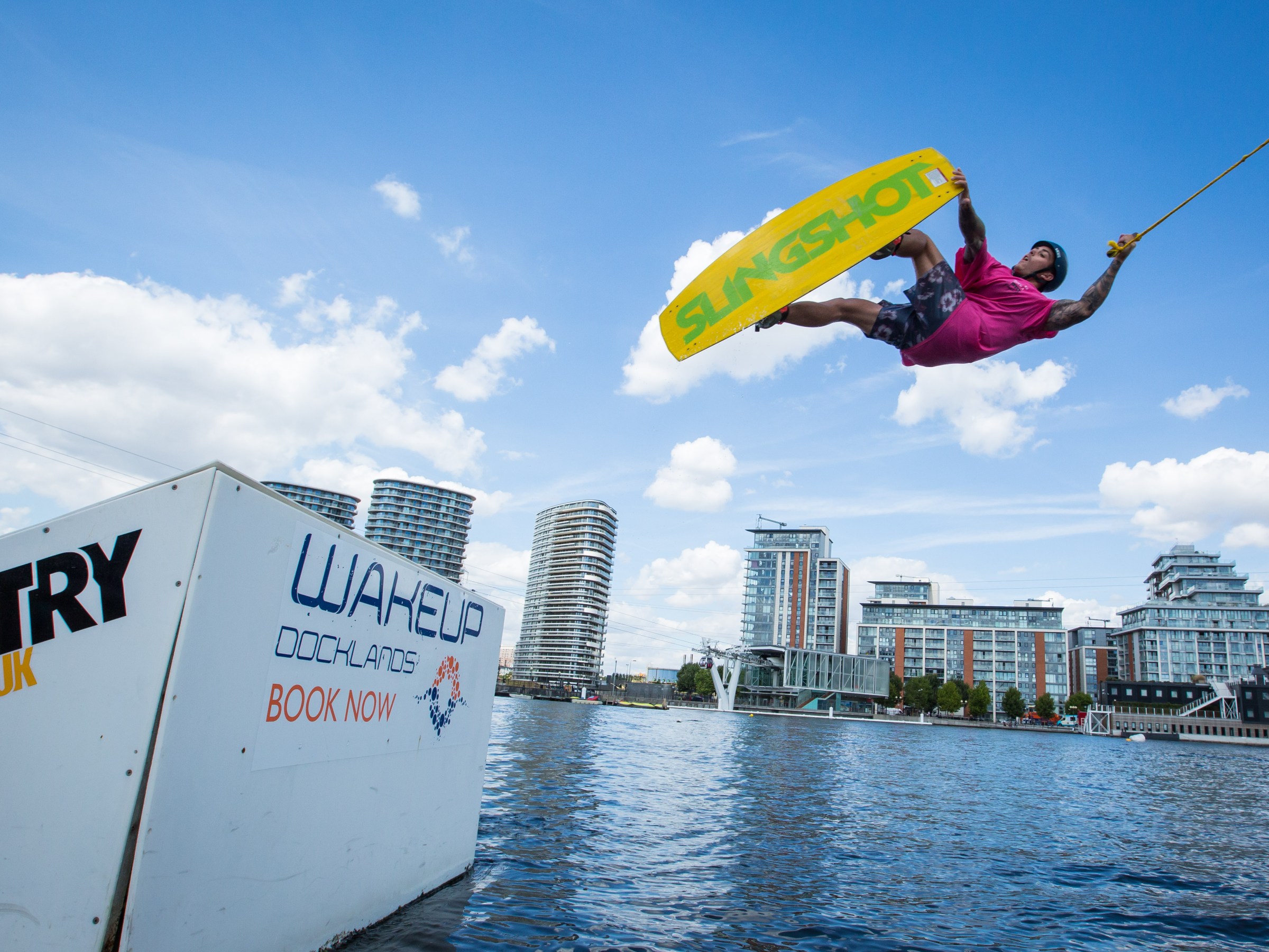 Person wakeboarding, airborne above water with city buildings in the background.