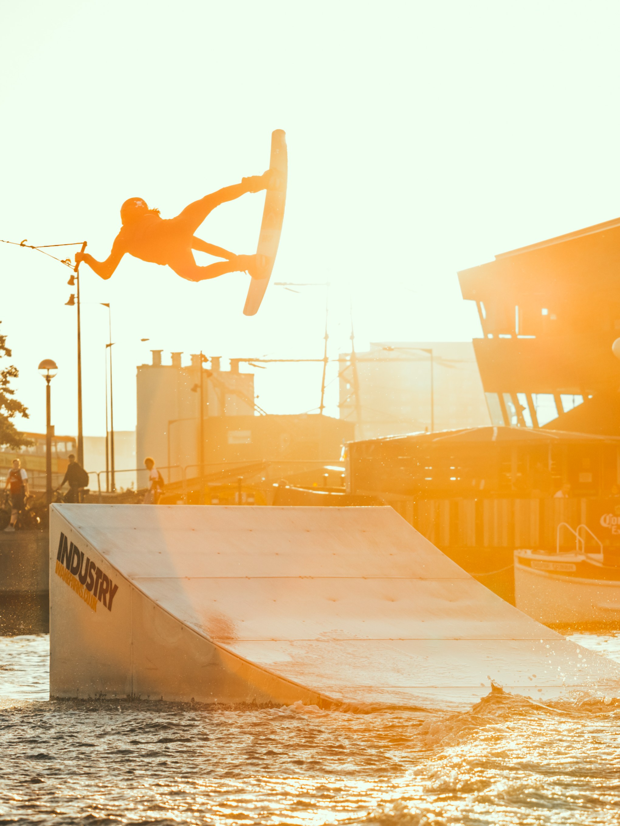 Person wakeboarding mid-air during sunset near a ramp on water.