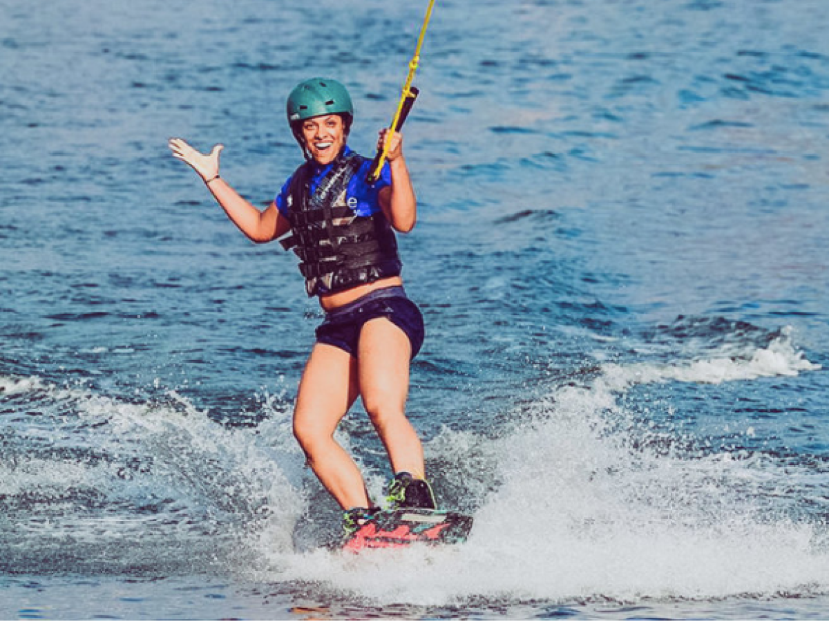Person wakeboarding on water, smiling, wearing blue helmet and black life vest.