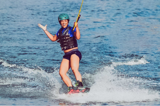 Person wakeboarding on water, smiling, wearing blue helmet and black life vest.