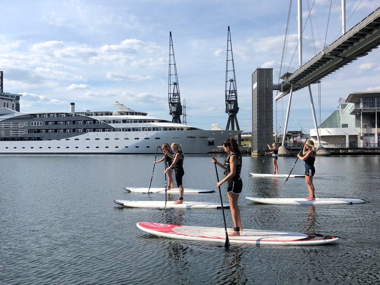 People paddleboarding on a river with a bridge and buildings in the background.