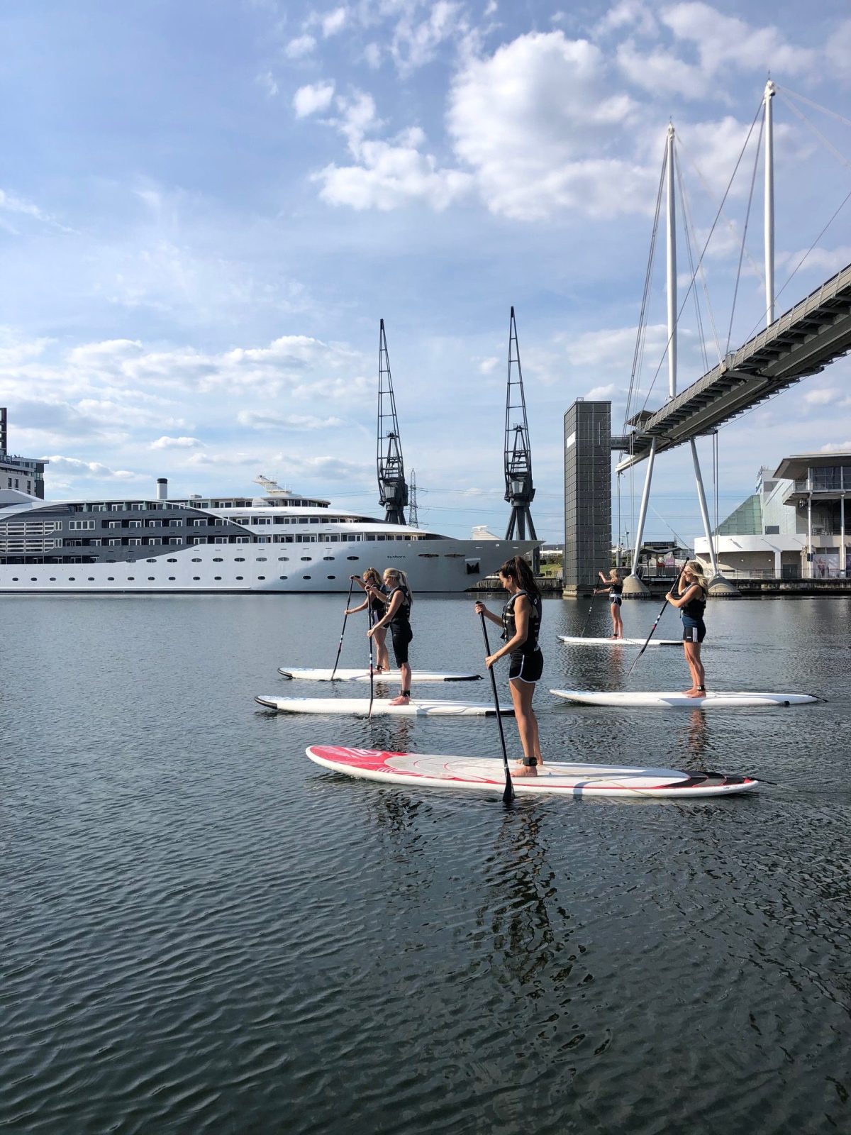 People paddleboarding on a river with a bridge and buildings in the background.