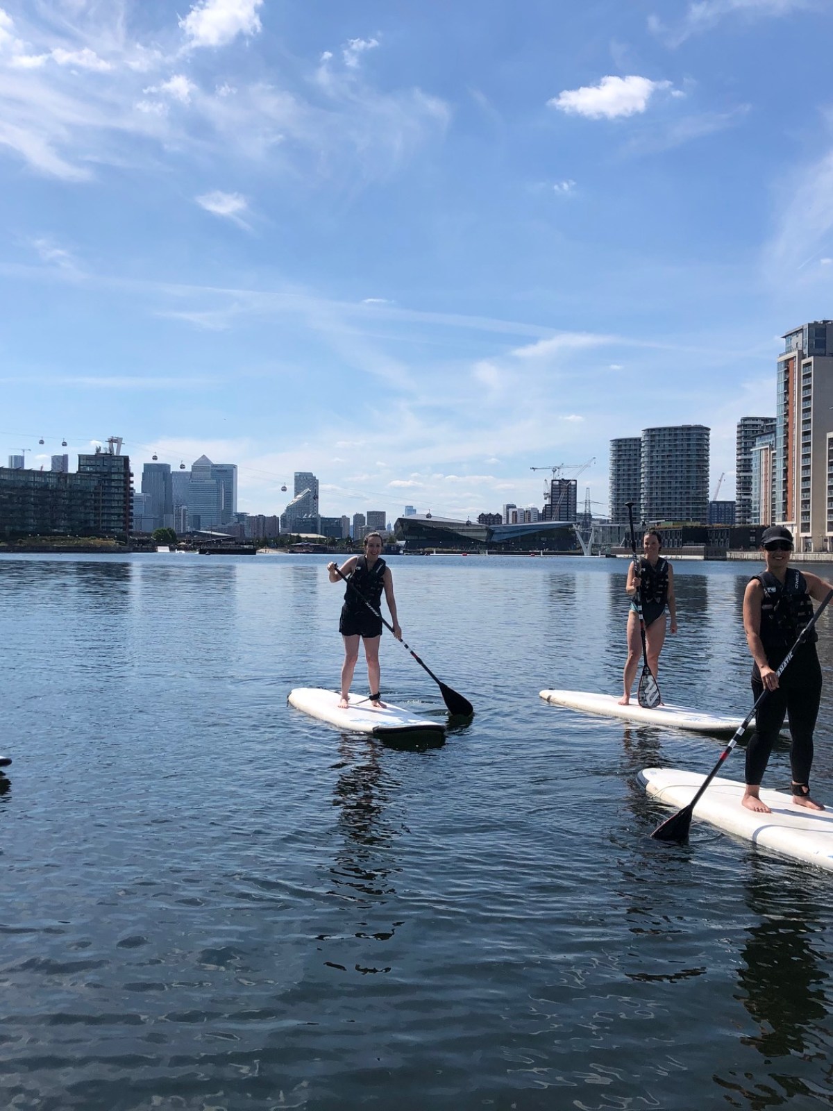 Four people paddleboarding on a calm urban waterway under a blue sky.