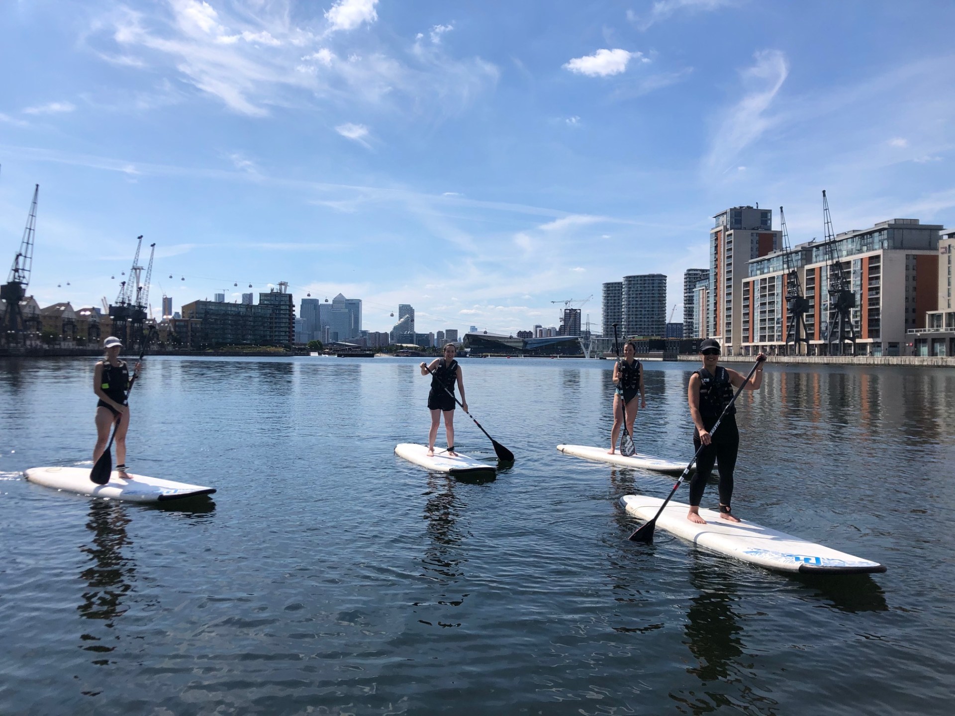 Four people paddleboarding on a calm urban waterway under a blue sky.