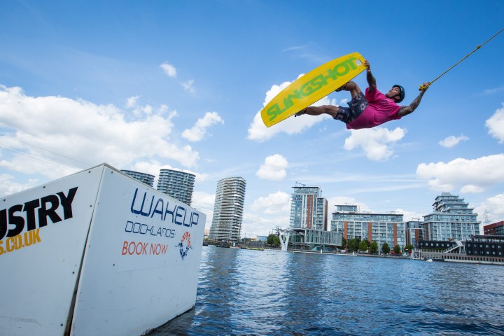 Person wakeboarding, performing a jump over water with a vibrant cityscape background.