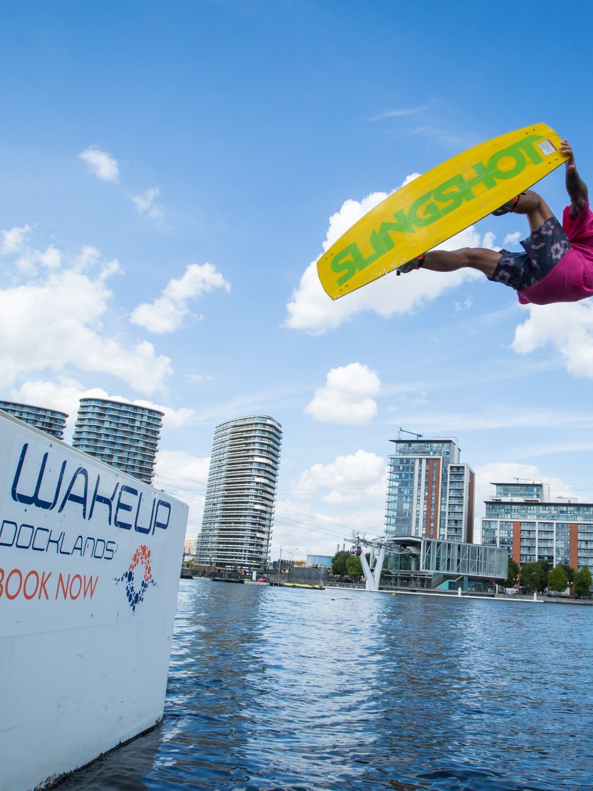 Person wakeboarding, performing a jump over water with a vibrant cityscape background.