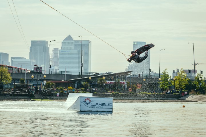 Person wakeboarding, performing a jump with city skyline in background.
