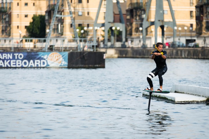 Person wakesurfing in a body of water near industrial buildings.