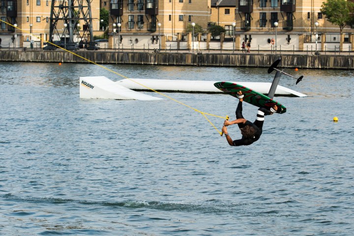 Person wakeboarding, performing a flip over water near a dock.