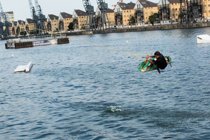 Person wakeboarding on water with cranes and buildings in the background.