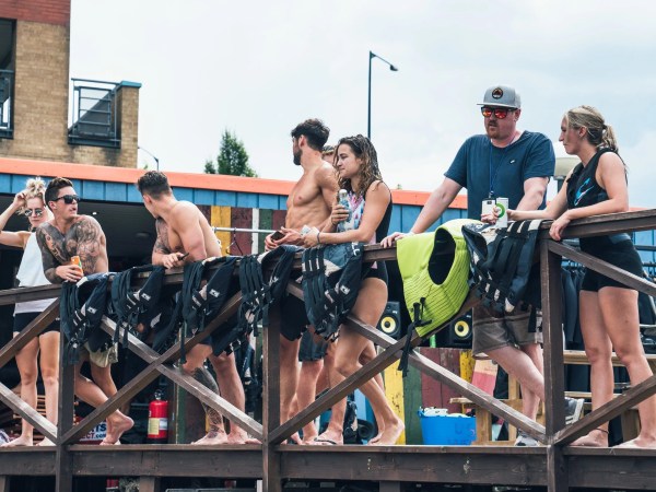 Group of people in swimwear standing by a wooden railing with life vests.